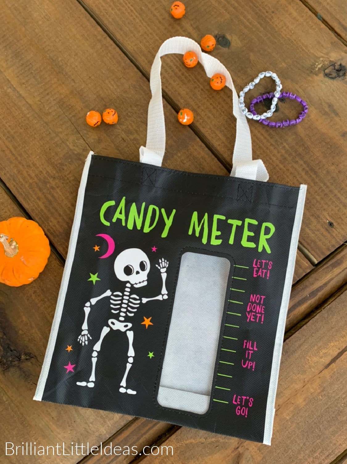 On a wooden background with pumpkin candy scattered around a cute trick or treat bag that says Candy Meter. A small pumpkin sets to the side. 